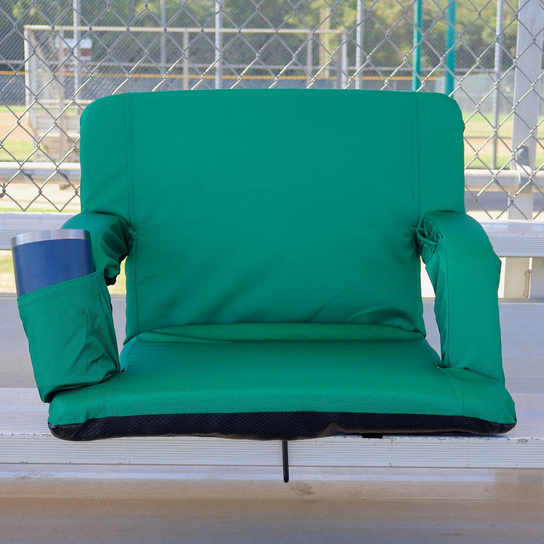 A green stadium-style spectator chair with padded armrests and a side cup holder, shown on outdoor bleachers with a chain-link fence in the background.